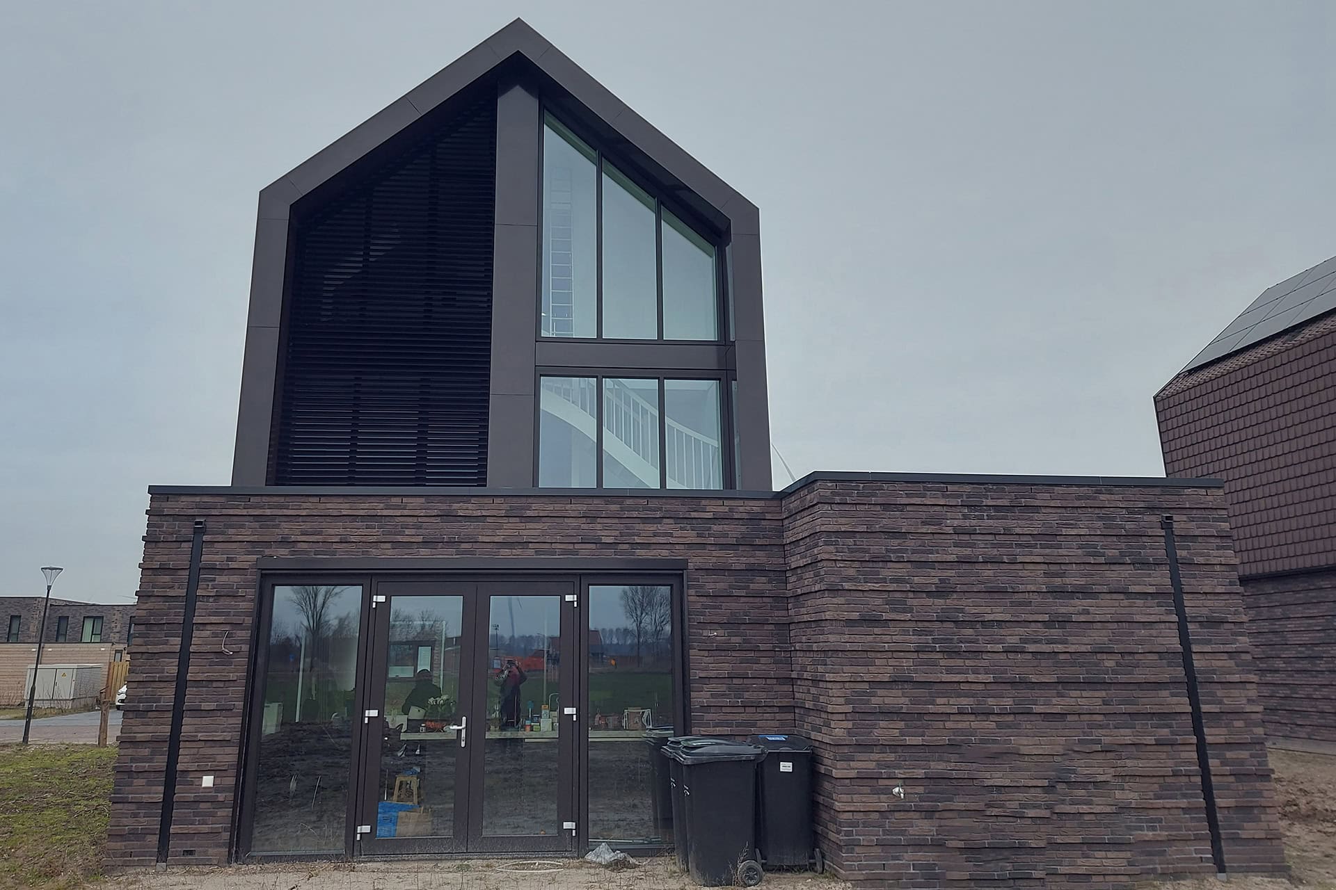 Groot trapeziumvormig raam met kantelbare lamellen in open stand op de 1ste en 2de verdieping van de woning