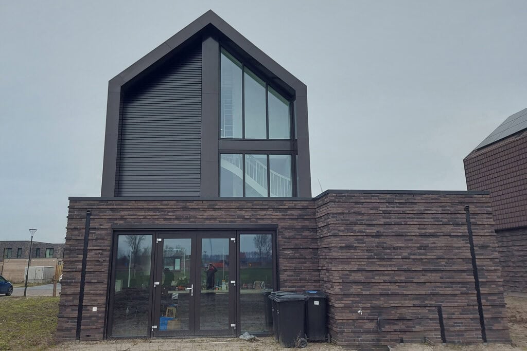 Groot trapeziumvormig raam met kantelbare lamellen in gesloten stand op de 1ste en 2de verdieping van de woning